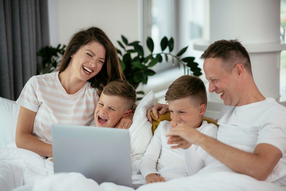 A family is sitting on a bed using a laptop computer.