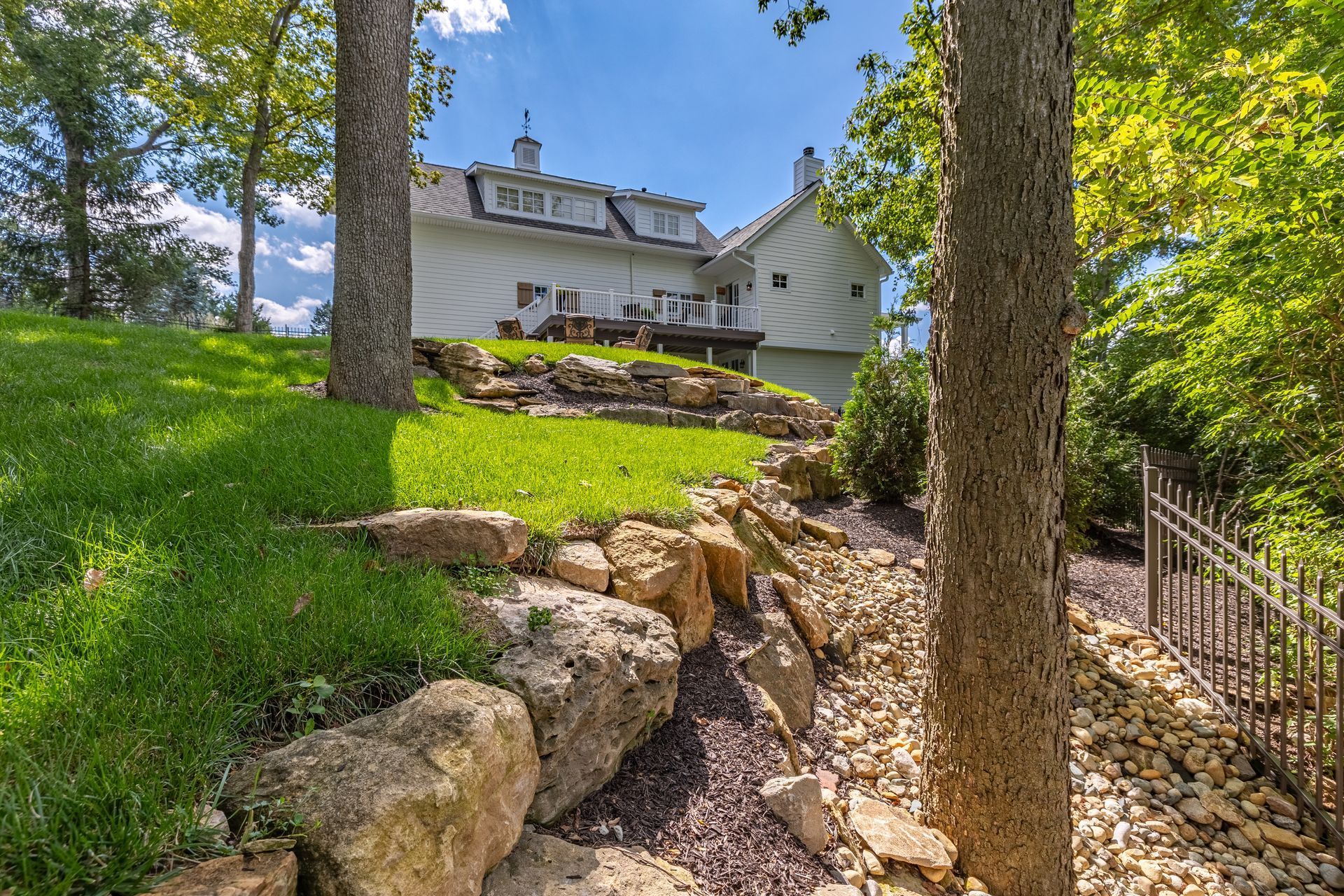 A large white house is sitting on top of a hill surrounded by trees and rocks.