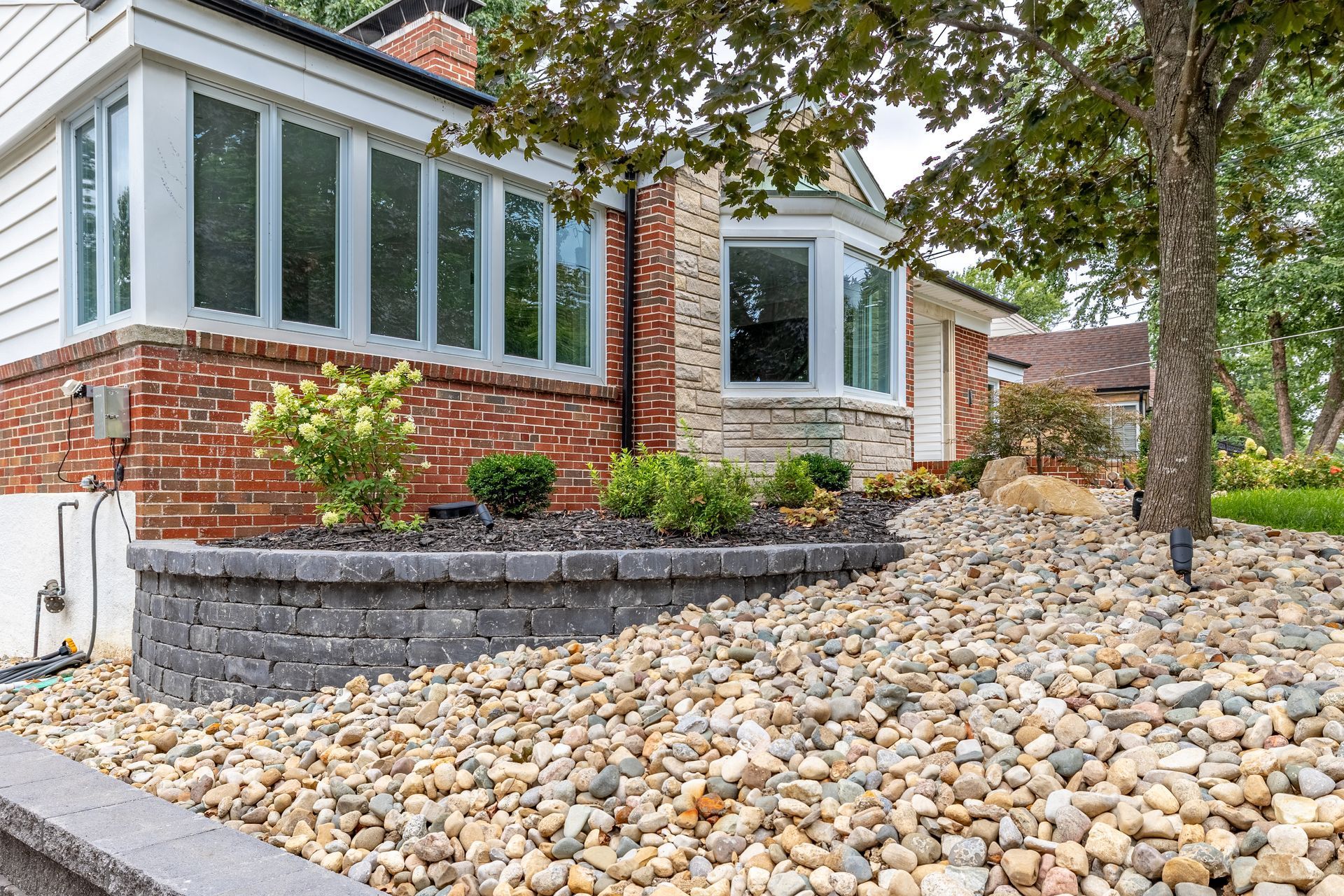 A large pile of rocks is in front of a brick house.