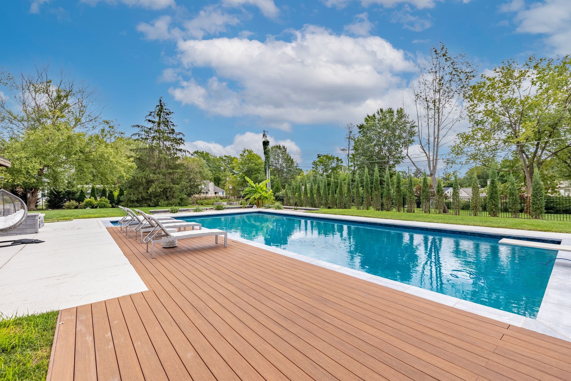 A large swimming pool with a wooden deck and chairs around it.