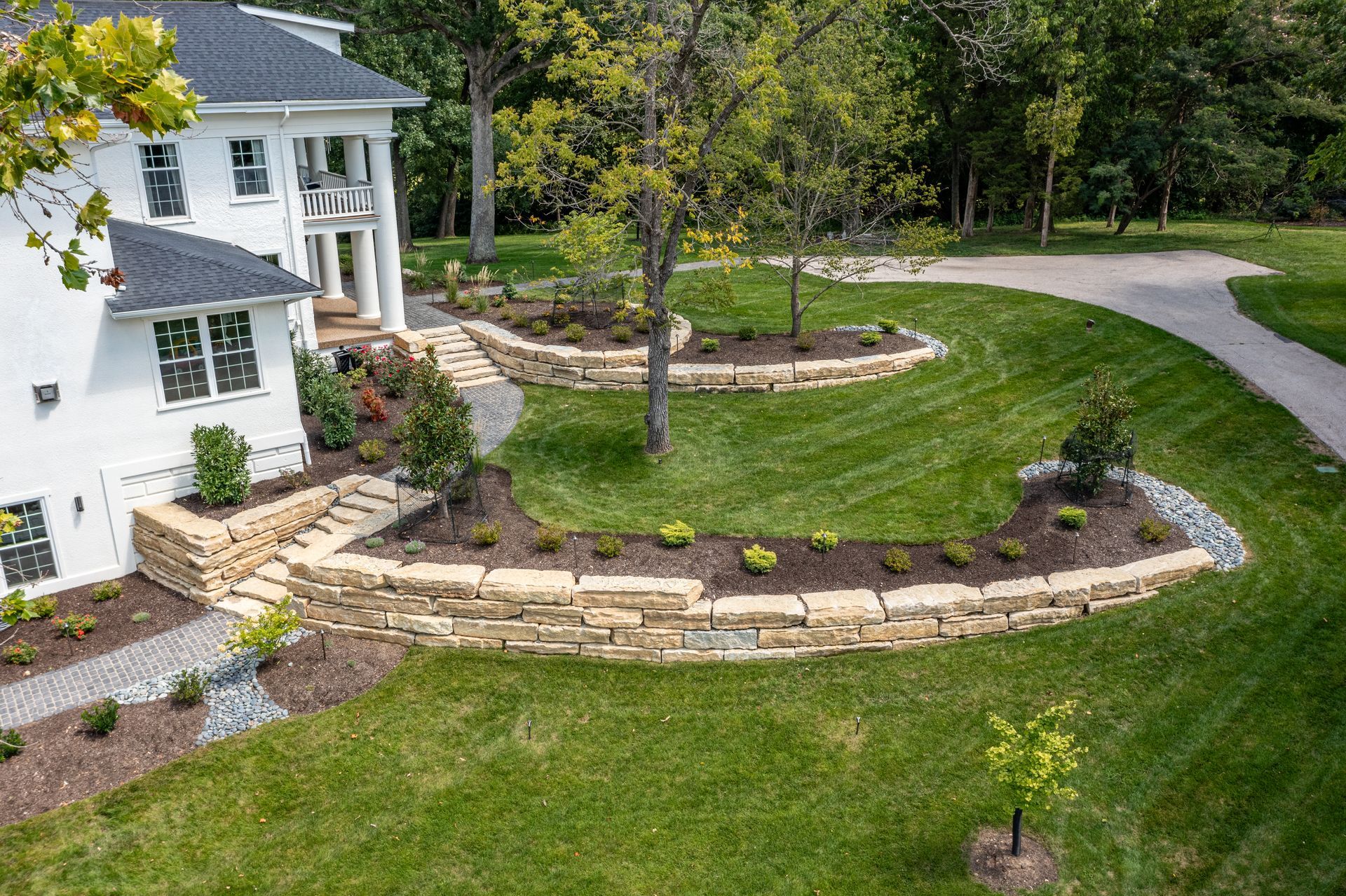 An aerial view of a large white house with a lush green lawn and a stone wall.