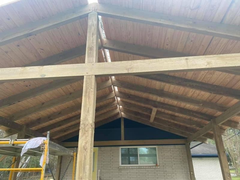 Wooden structure with angled roof beams. Brown planks form the ceiling over a brick building with a window.