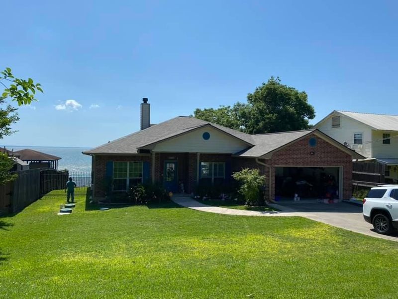 House with green lawn, blue shutters, and a view of the water under a clear blue sky.