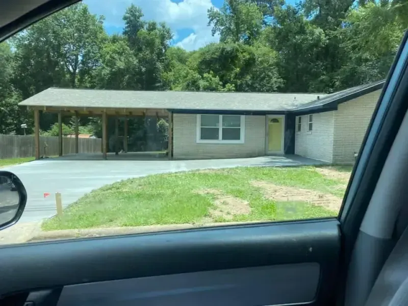 Exterior view of a house with a carport and yellow door, on a sunny day.