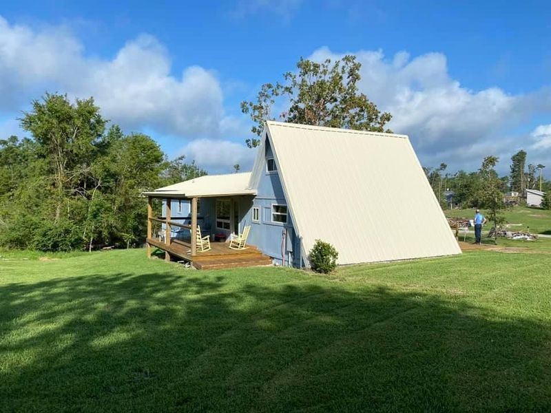 Blue A-frame house with a covered porch on a grassy lawn under a blue sky.