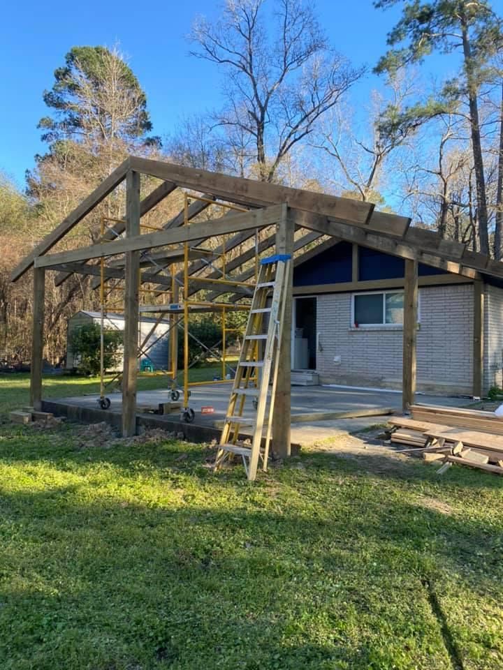 Construction of a wooden pergola attached to a brick building; ladder, supports, and materials are visible in yard.