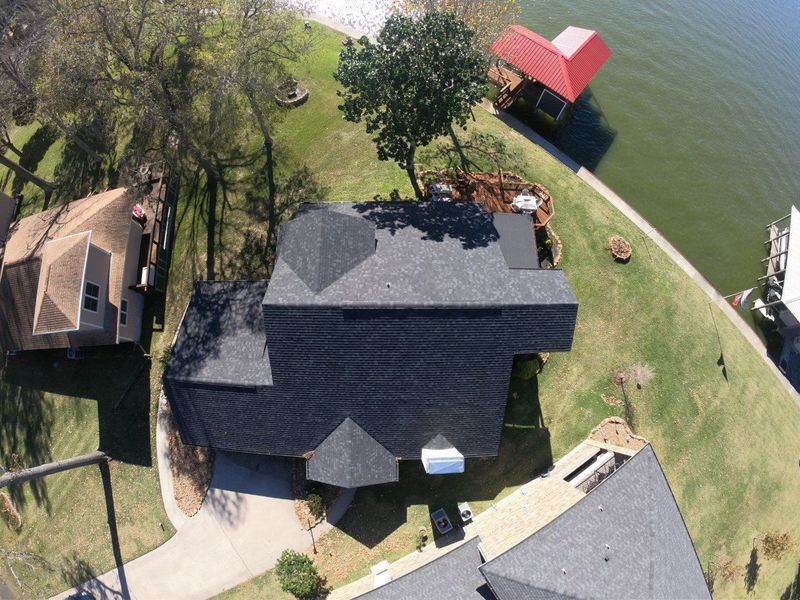 Overhead view of a house with a dark roof near a lake, next to a dock with a red roof.