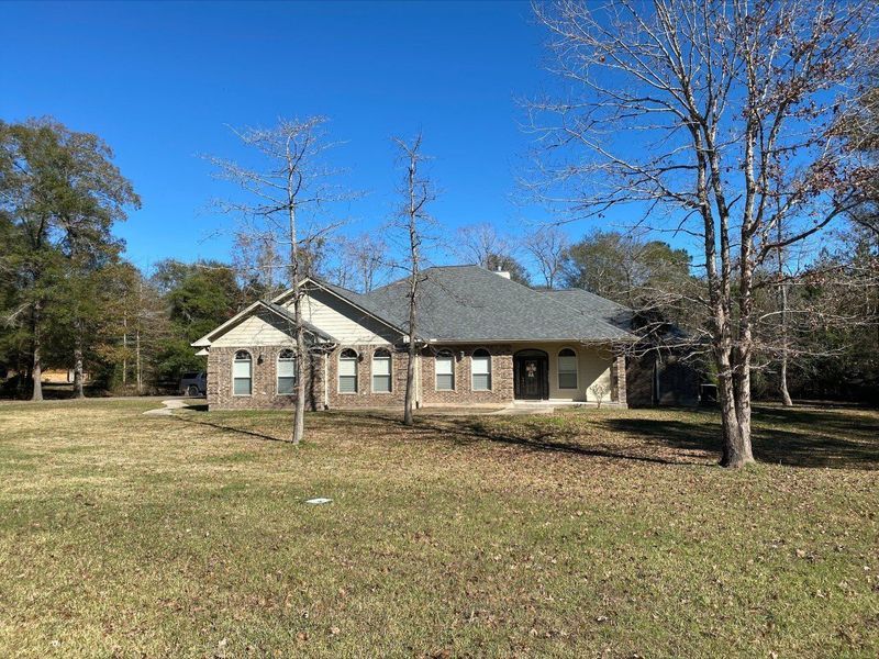 Ranch-style house with gray roof and brick facade, set in a grassy yard under a blue sky.