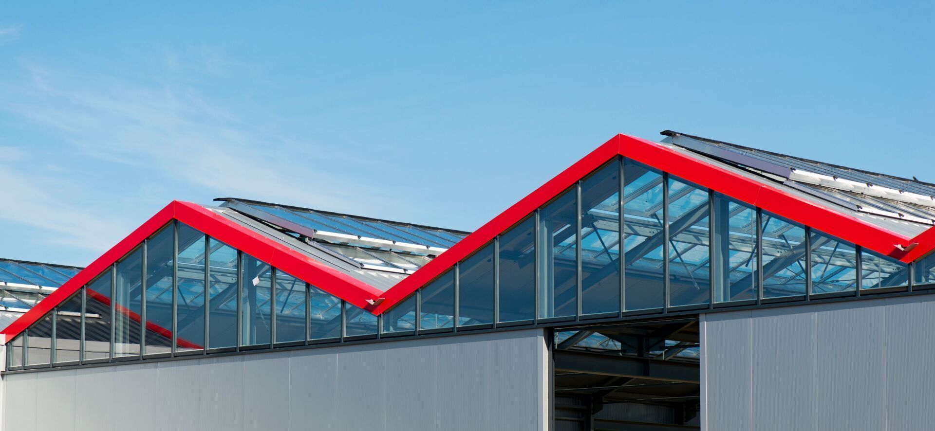 Red-roofed building with glass windows, against a blue sky.