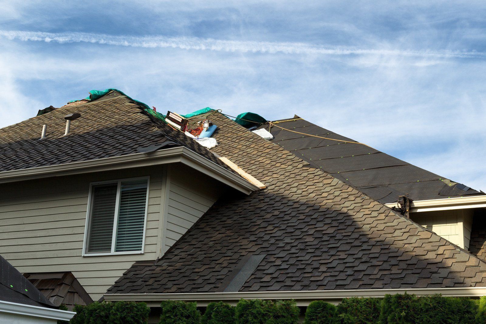 Damaged roof with missing shingles; blue sky and visible vapor trail in background.