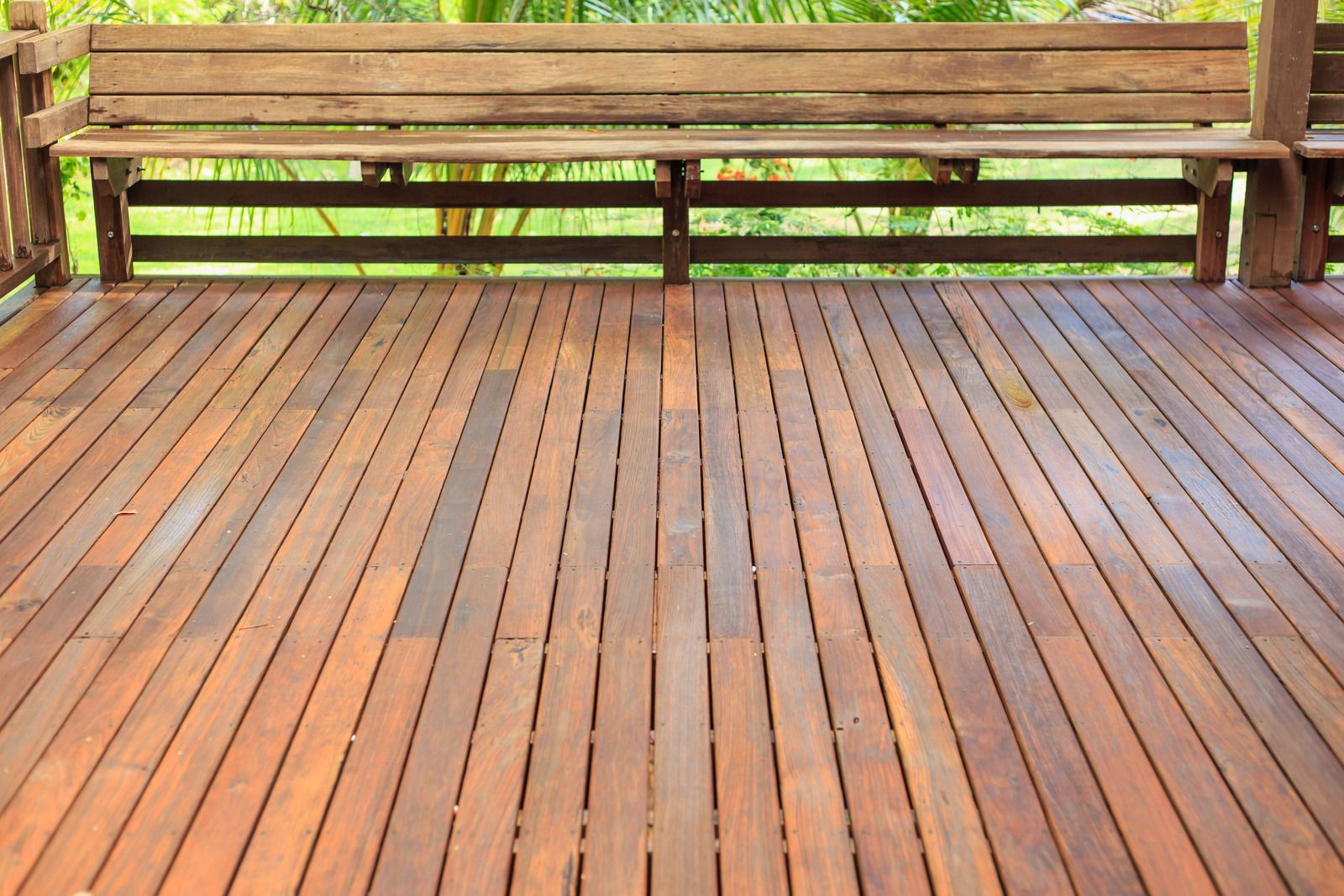 Wooden deck with a built-in bench, with a blurred green background.
