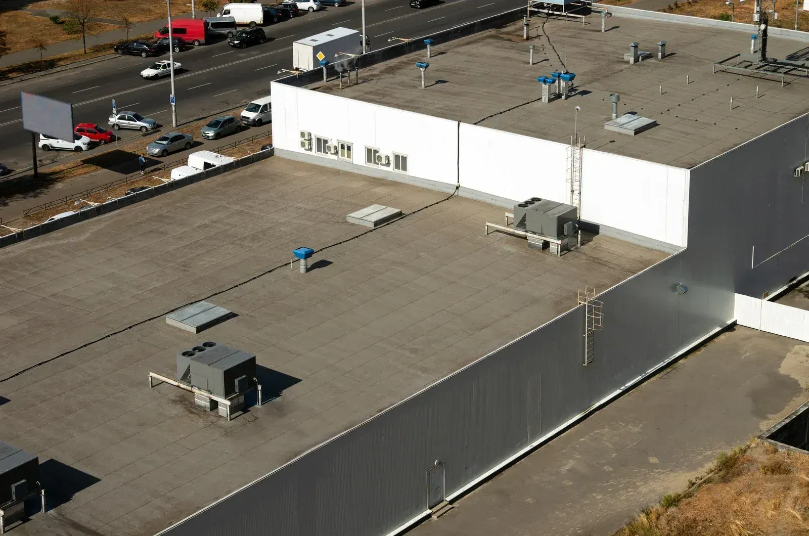 Aerial view of a commercial building rooftop with HVAC units, vents, and a road with cars.