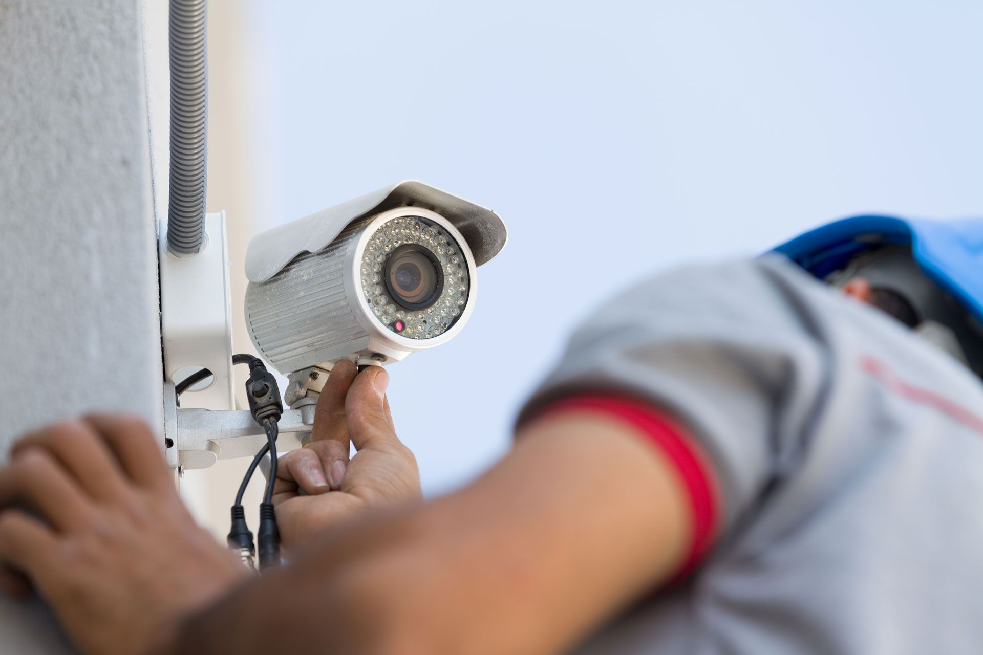 A man is installing a security camera on the side of a building.