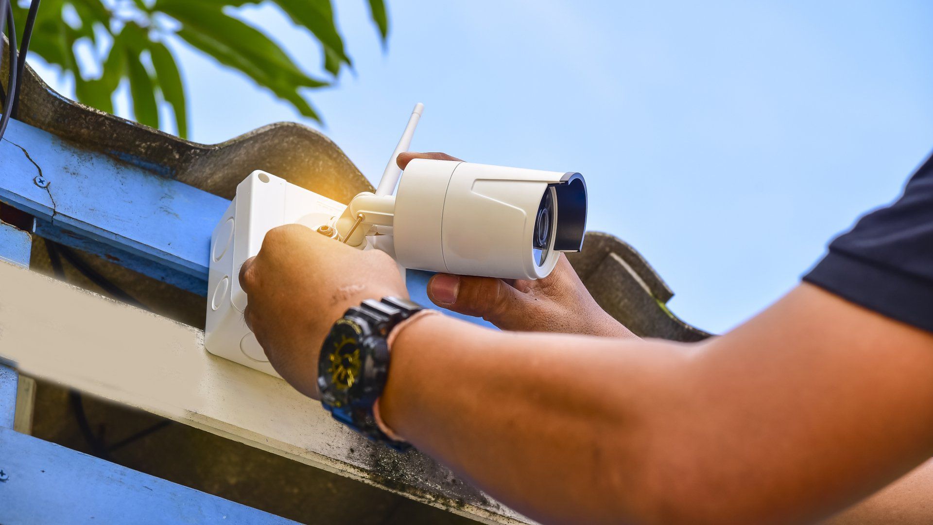 A man is installing a security camera on the roof of a building.