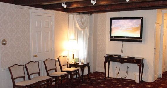 Waiting room with chairs, TV, and table; floral wallpaper and dark wood trim.