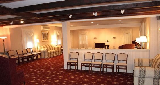 Funeral home interior with seating, red carpet, and open alcove.