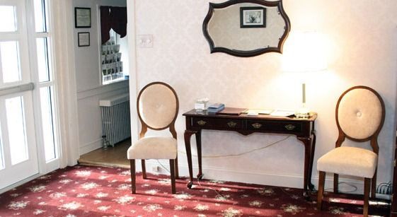 An entryway with two chairs, table, mirror, and red floral carpet.