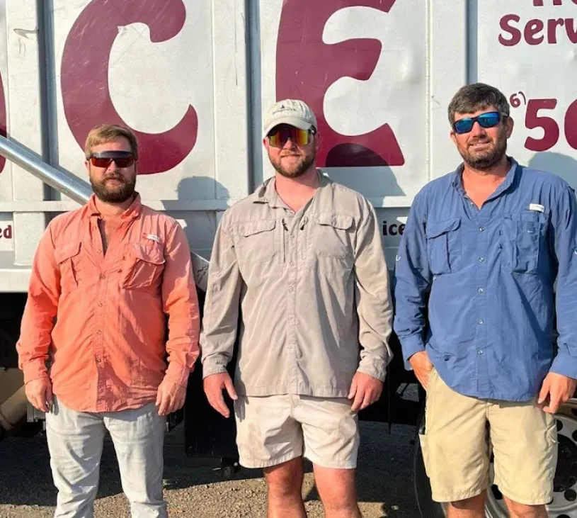 Three men standing in front of a truck that says ice