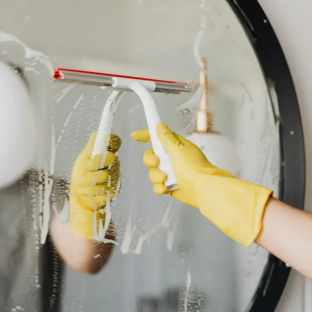 Person wearing yellow gloves cleaning a round mirror with a squeegee.