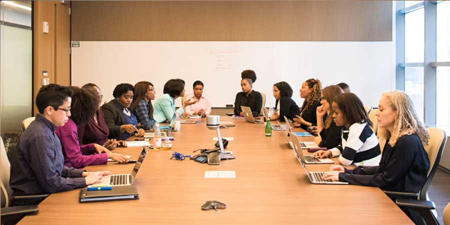 Un groupe de personnes sont assises à une longue table avec des ordinateurs portables.