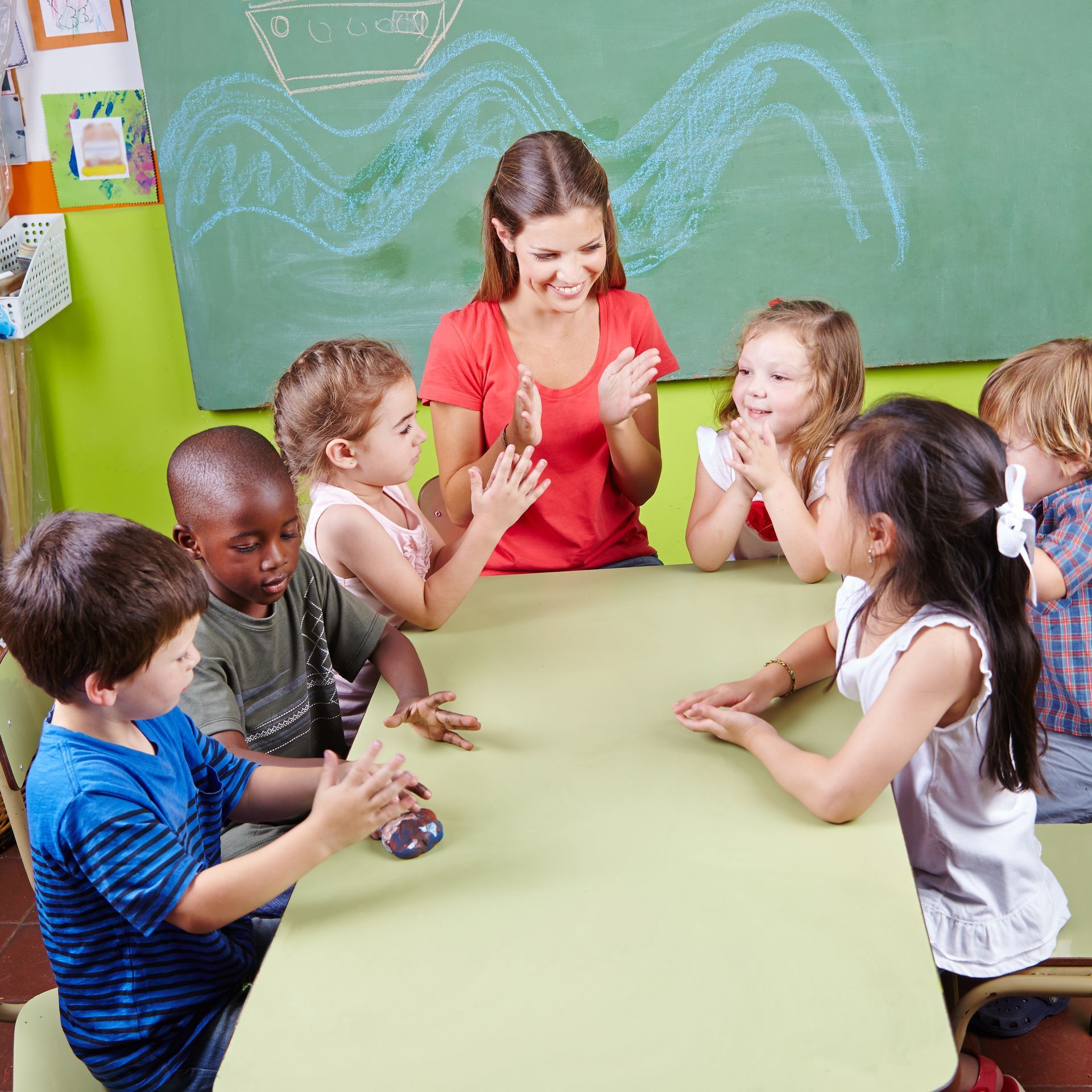 Image d'une enseignante à une table intéragissant avec 6 enfants.