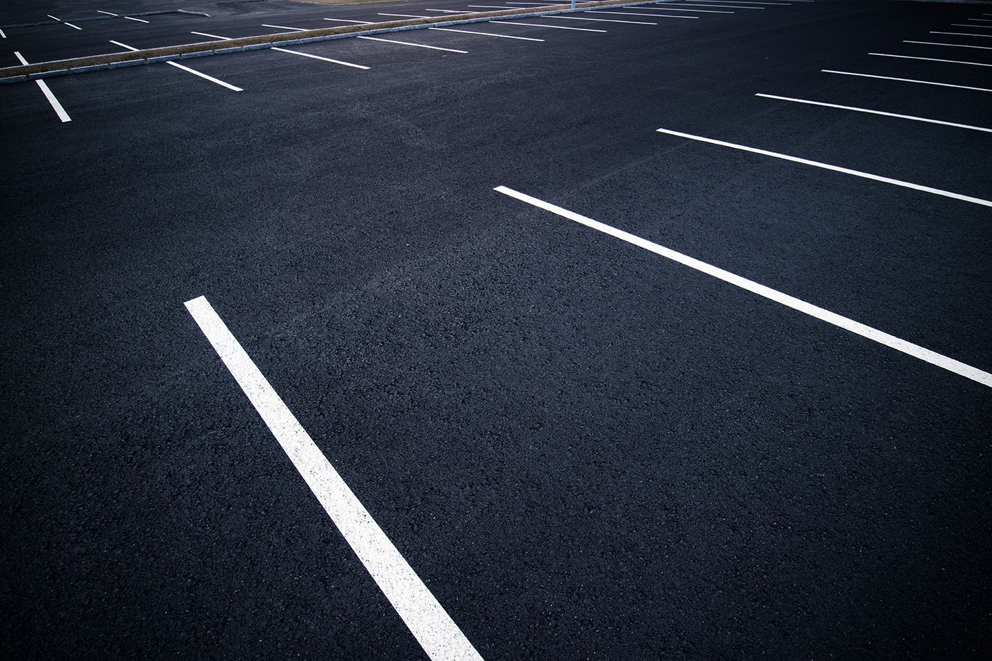 Black asphalt parking lot with white painted parking space lines.