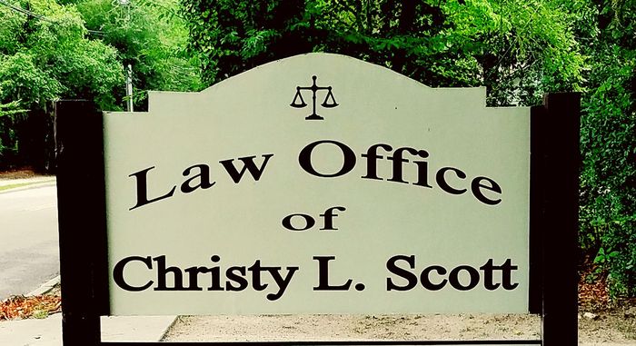 Law Office sign for Christy L. Scott with scales icon, set against green trees