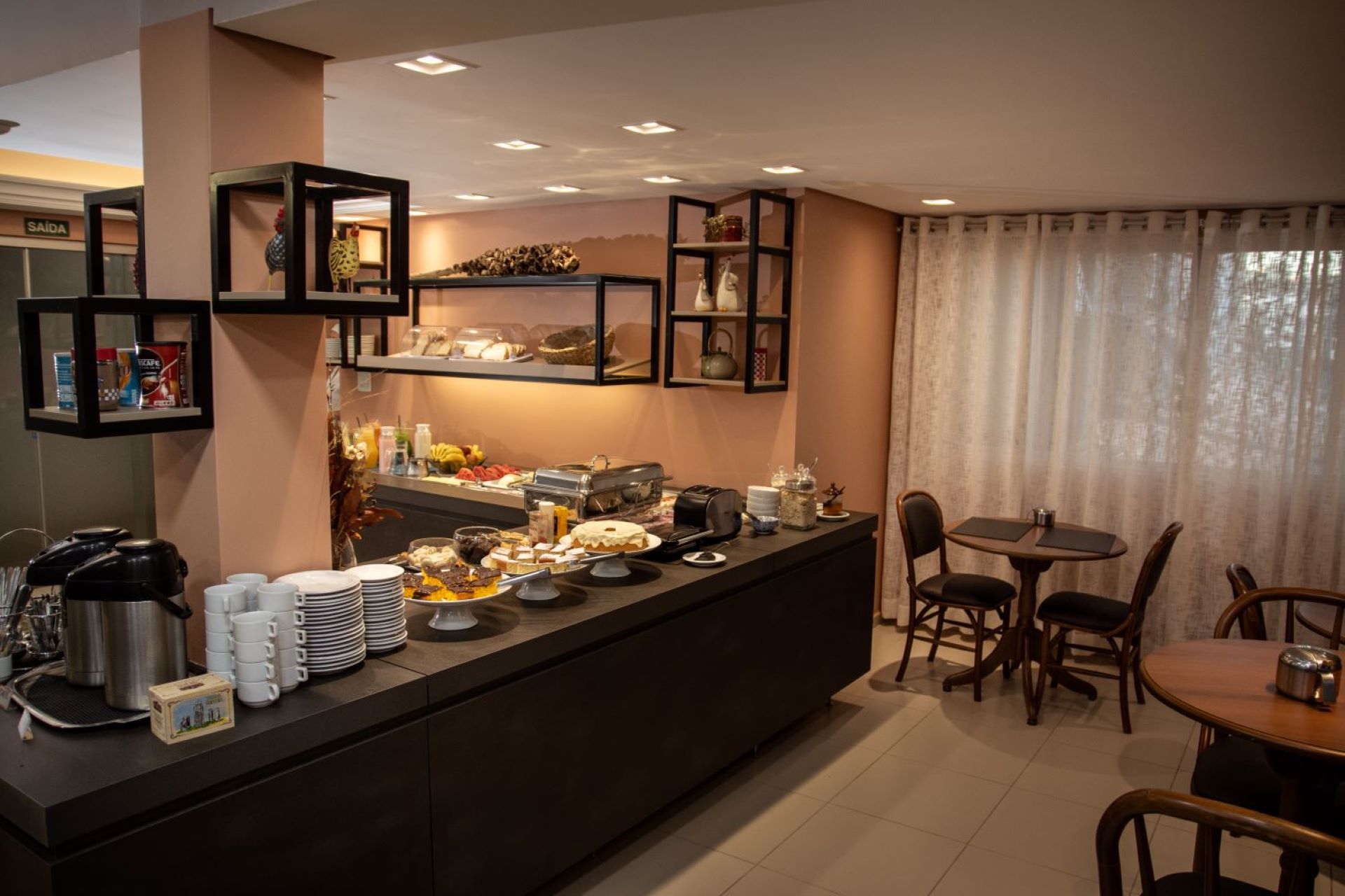 Há um buffet no meio da sala com mesas e cadeiras.