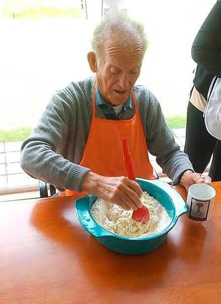 Un hombre mayor con delantal está mezclando algo en un recipiente.