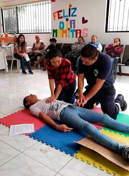 Un grupo de personas está practicando primeros auxilios a una mujer tendida en el suelo.