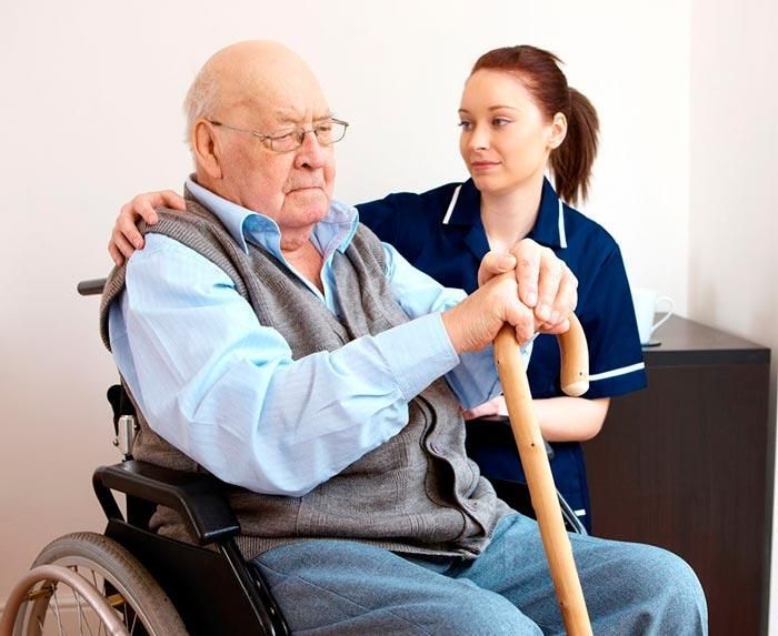 Un anciano en silla de ruedas está siendo ayudado por una enfermera.