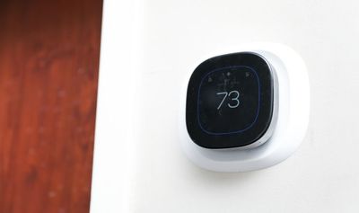 A smart thermostat is hanging on a white wall.