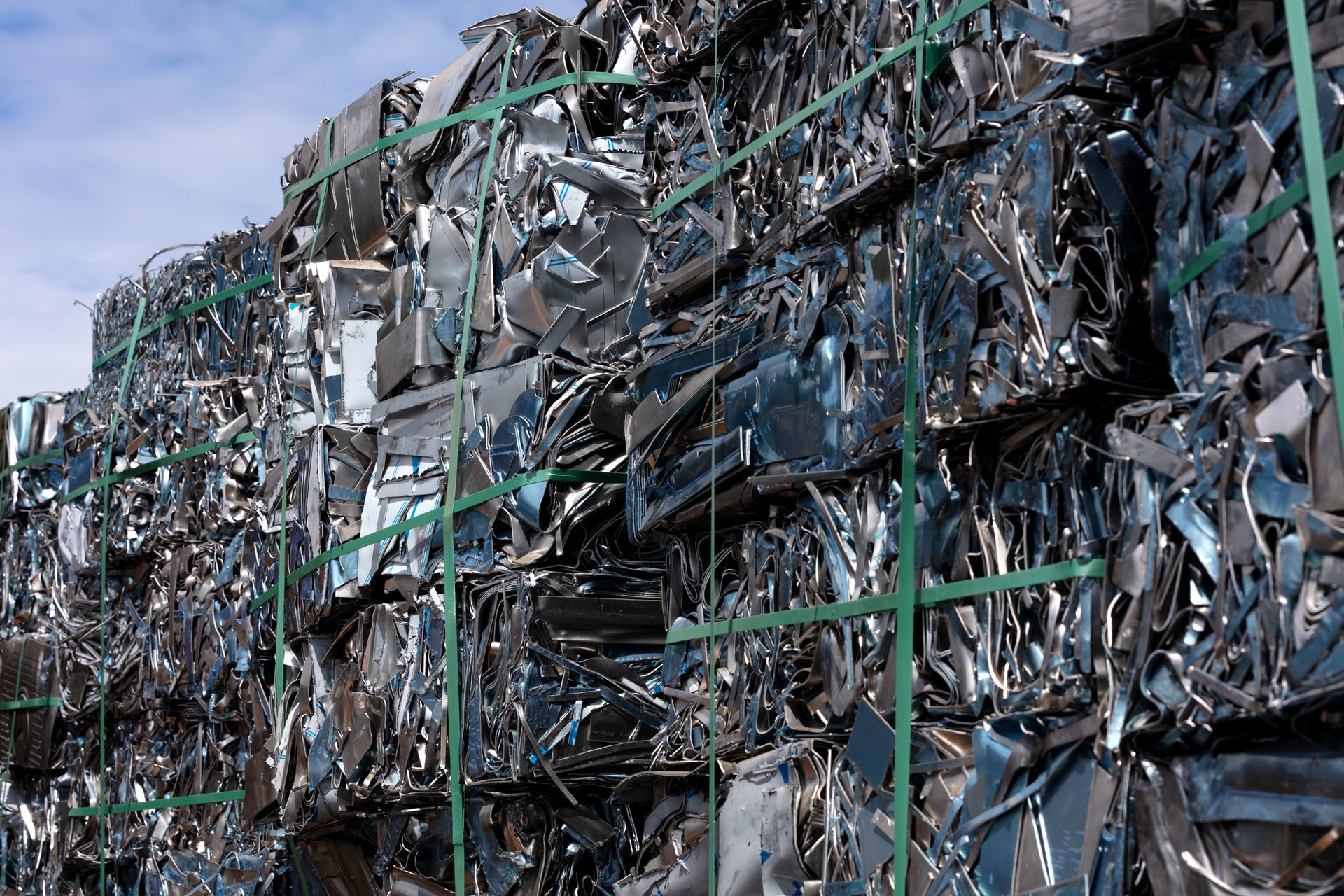 Compressed metal scrap bundles secured with green straps at a recycling facility.