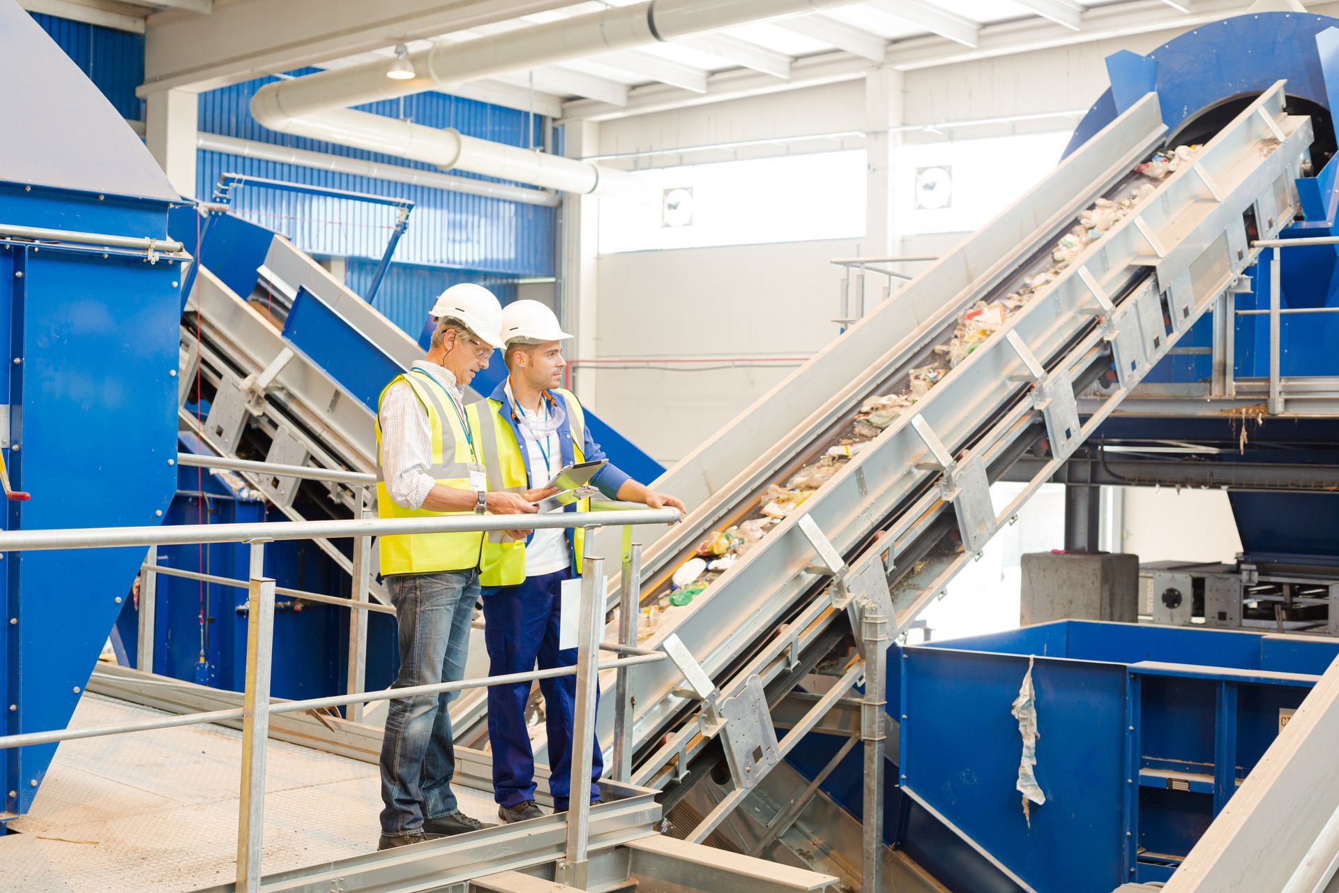 A pair of workers talk while standing on the railing of a recycling center. A pair of workers talk while standing on the railing of a recycling center.