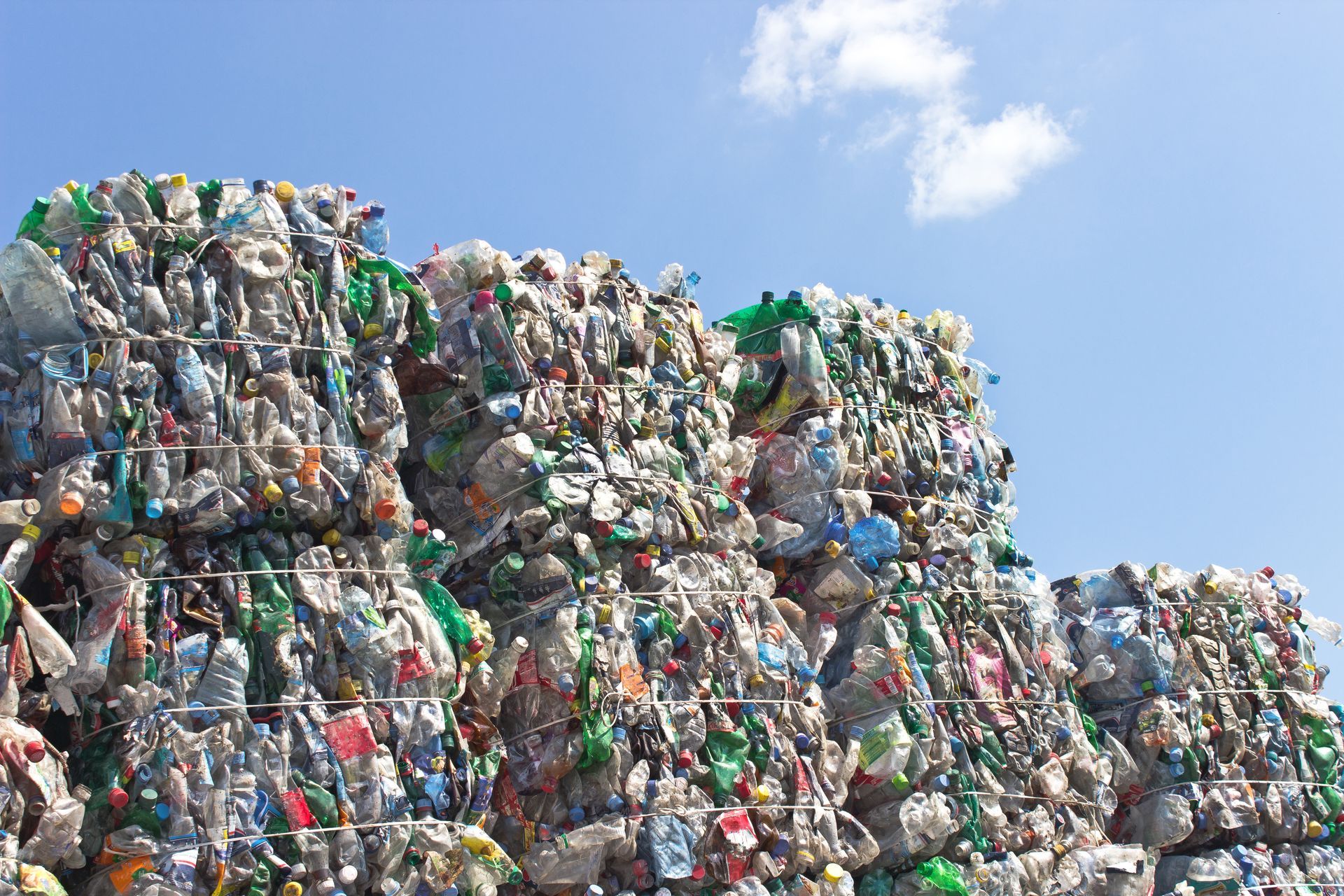 Large bundles of compressed plastic bottles stacked outdoors at a recycling facility.