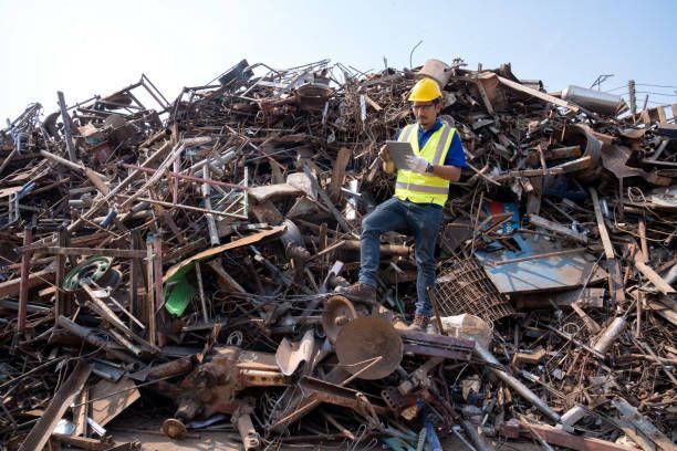 A man is on top of a bunch of steel in a recycling plant.