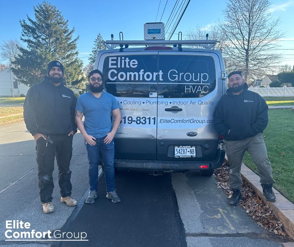 Three technicians stand outside by a silver Elite Comfort Group HVAC service van on a sunny day.