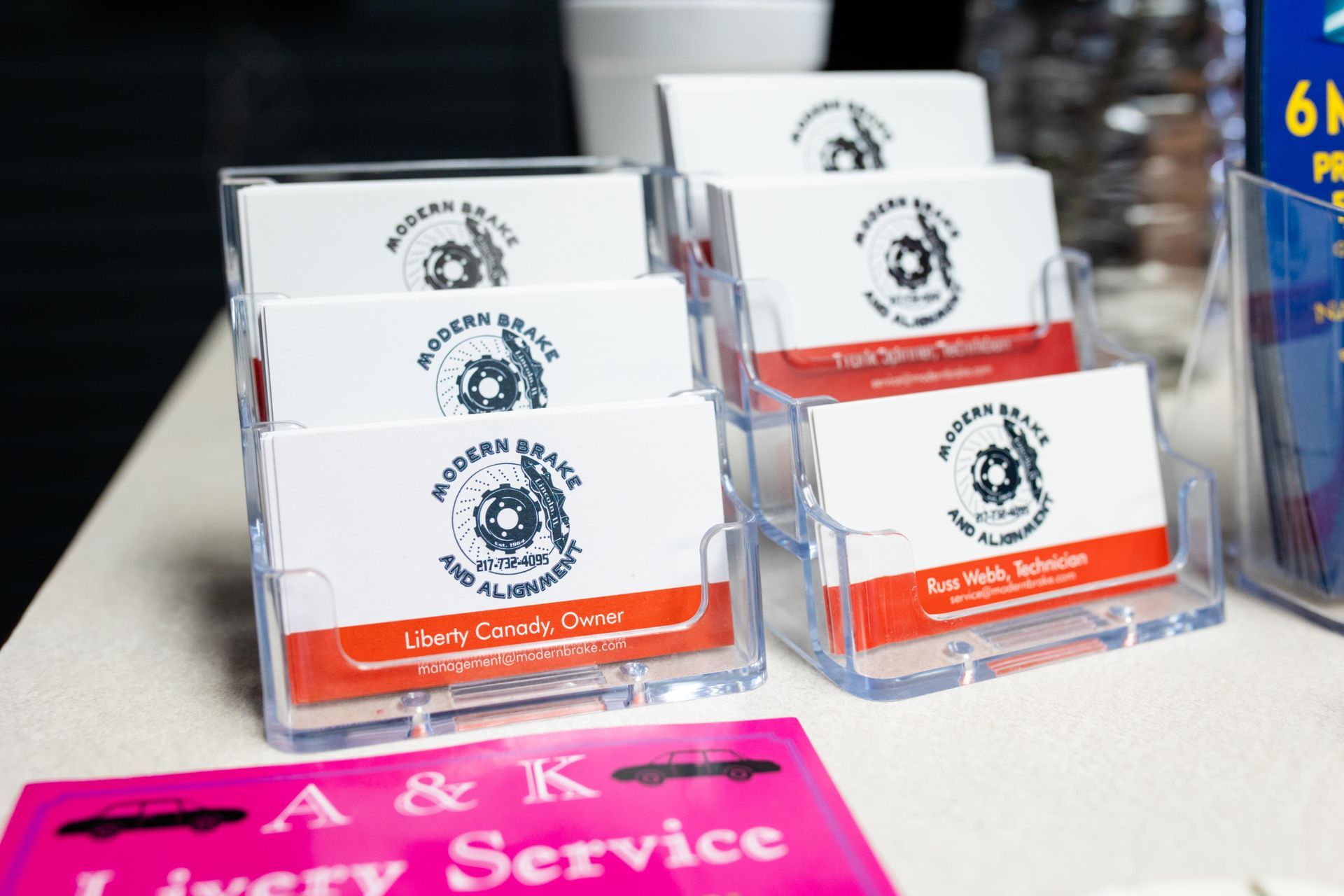 Business cards in plastic holders, with a logo and red and white details, displayed on a table | Modern Brake & Alignment