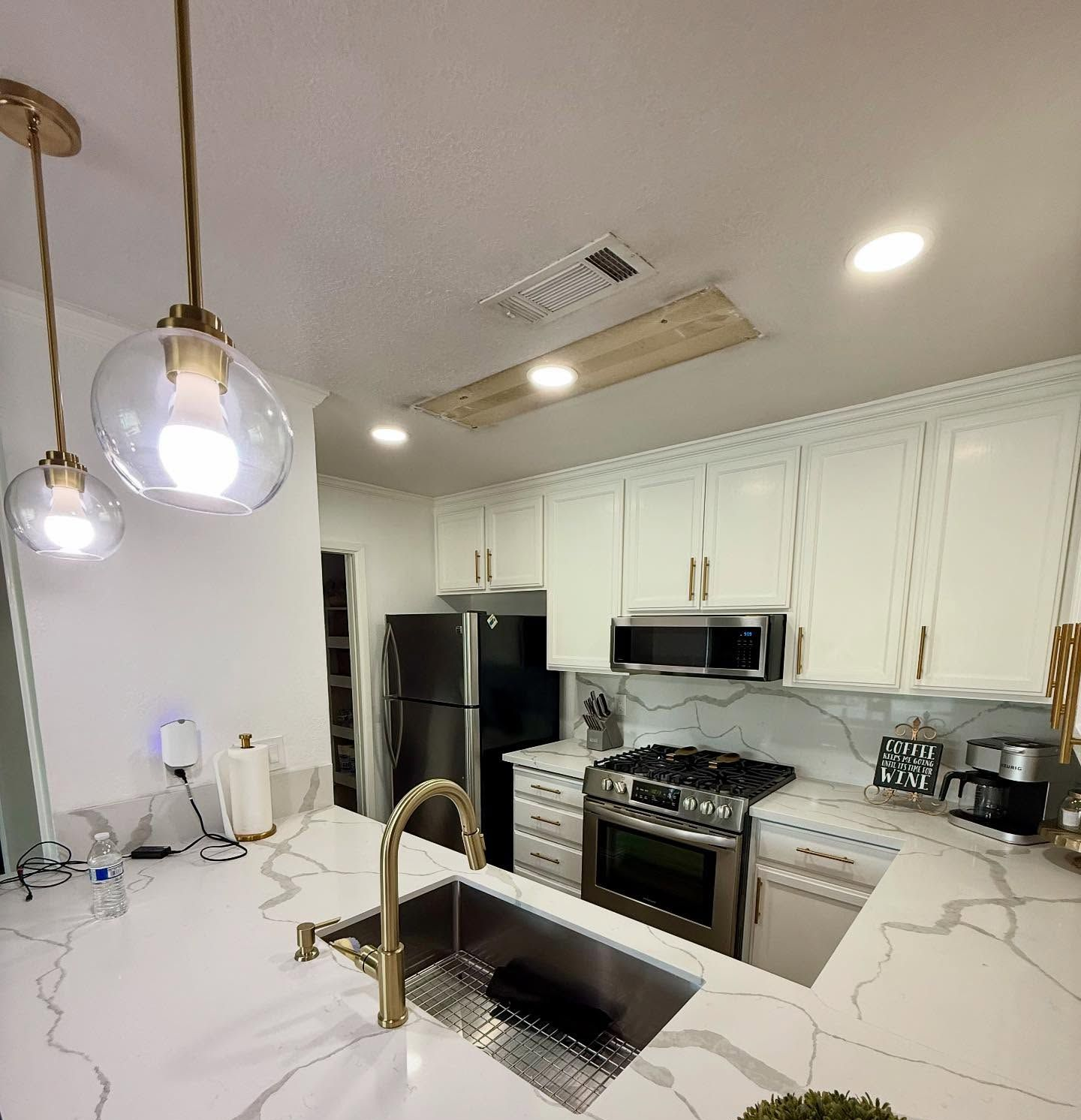 Modern kitchen with white cabinets, gold fixtures, marble countertops, and stainless steel appliances.