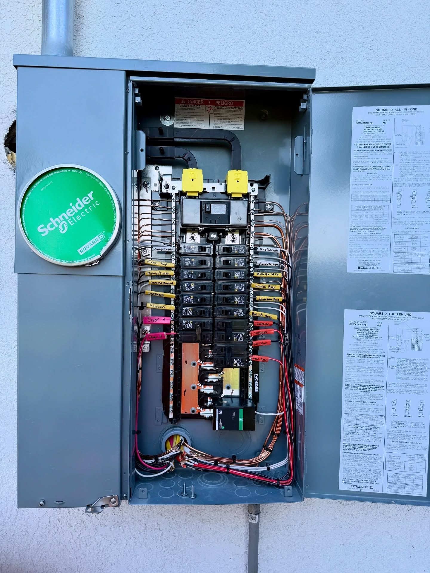 Outdoor electrical panel with circuit breakers, wires, and a meter. Grey metal enclosure on a stucco wall.
