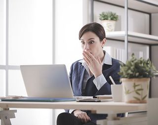 Young businesswoman having problems with her computer, she is staring shocked at the screen with an hand over mouth