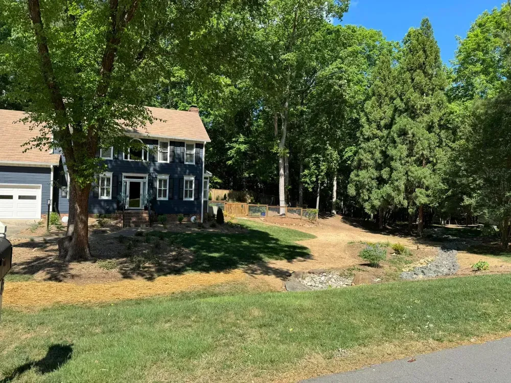 A blue house with a brown roof is surrounded by trees and grass.