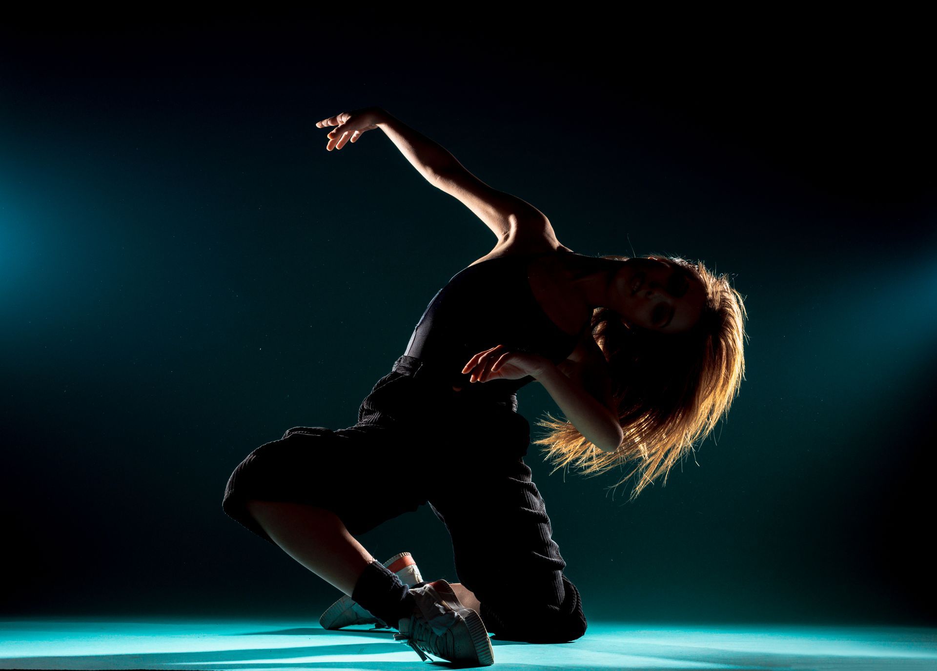 A woman is kneeling down and dancing in a dark room.