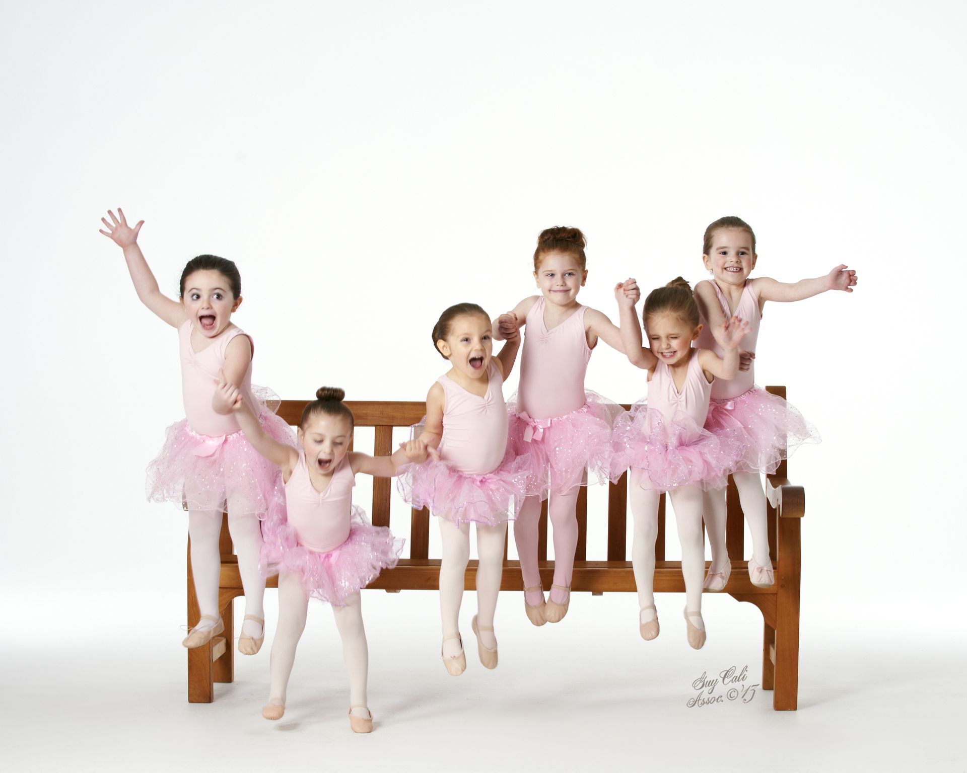 A group of young ballerinas are sitting on a wooden bench.