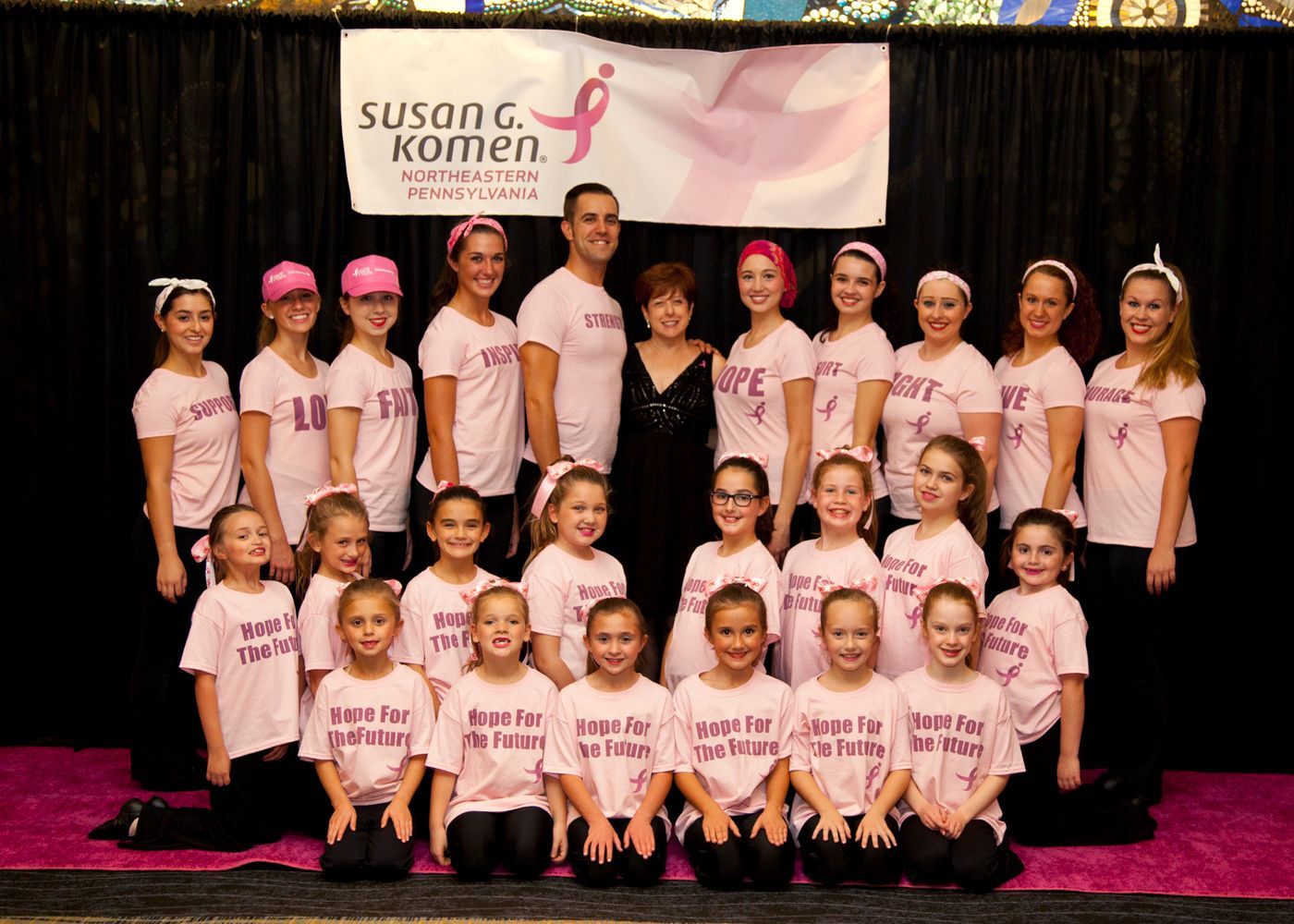 A group of young girls are posing for a picture in front of a susan komen banner