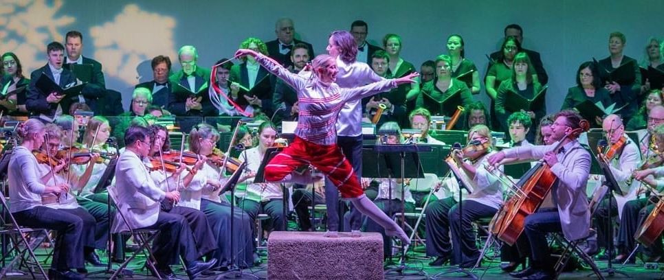A man is jumping in the air in front of an orchestra.