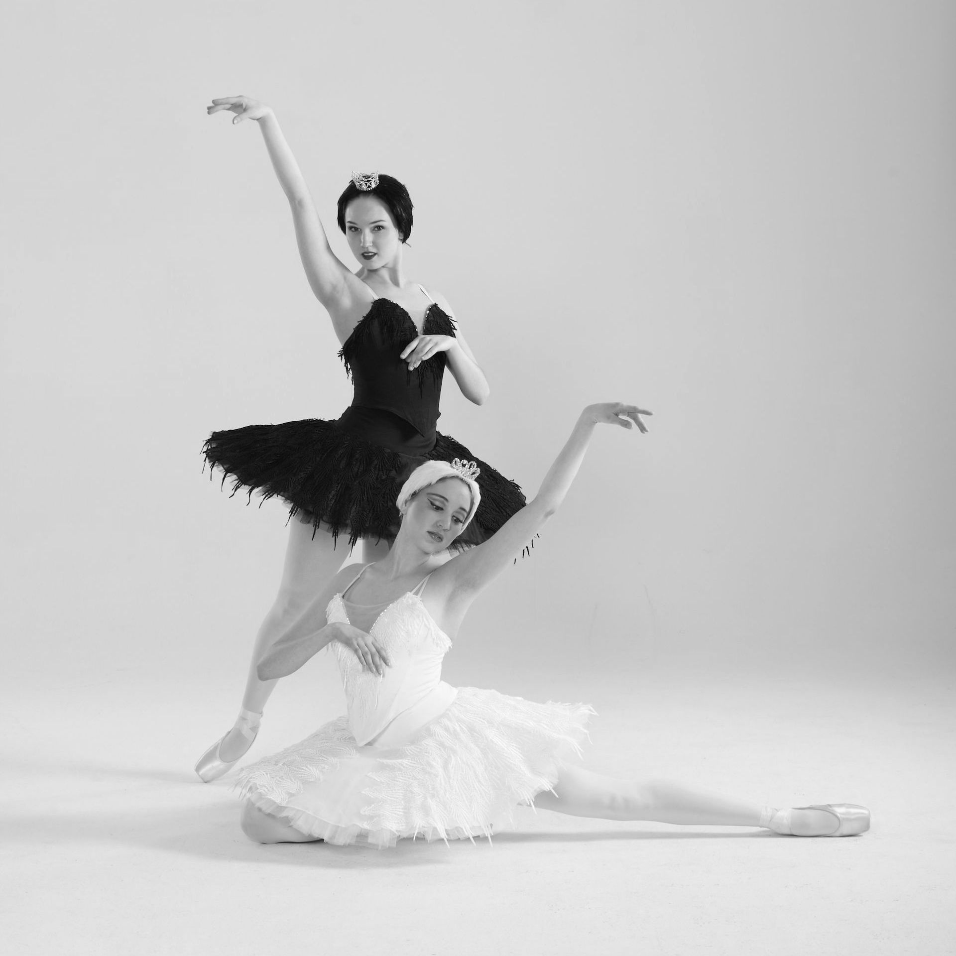 Two ballerinas are dancing together in a black and white photo.