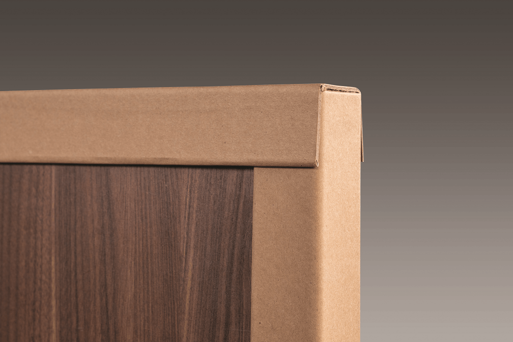 A close up of a cardboard corner on a wooden door.