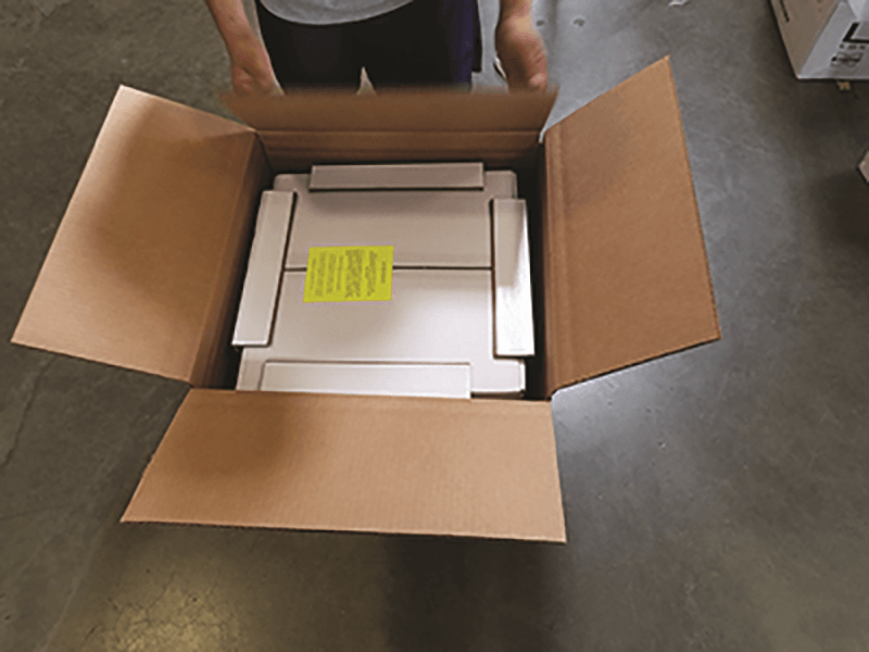 A person is opening a cardboard box with a yellow sticker on it