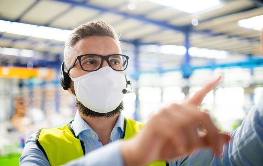A man wearing a mask and headphones is talking to another man in a warehouse.